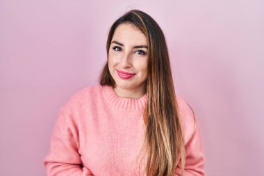 Young hispanic woman standing over pink background with hands together and crossed fingers smiling relaxed and cheerful. success and optimistic 