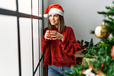 Genç İspanyol kız evde Noel ağacının yanında kahve içiyor..