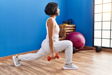 Genç Latin kadın gülümsüyor spor merkezinde dambıllar kullanarak kendine güven eğitimi alıyor.