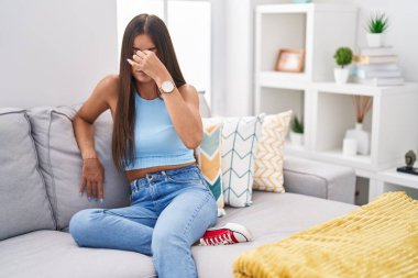 Genç esmer kadın evdeki kanepede oturuyor. Burnu ve gözleri ovuşturup yorgun ve baş ağrısı çekiyor. Stres ve hüsran kavramı. 