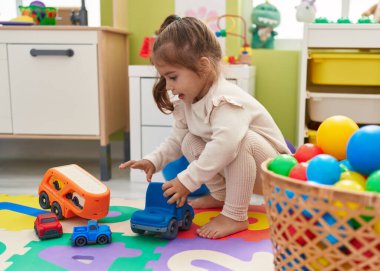 Anaokulunda yerde oturan sevimli İspanyol kız araba oyuncağıyla oynuyor.