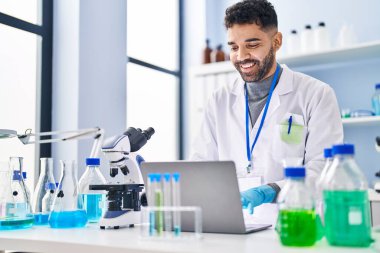 Laboratuvarda dizüstü bilgisayar kullanan Latin kökenli genç adam.