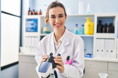 Young woman wearing scientist uniform using microscope at laboratory