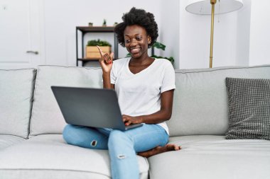African young woman using laptop at home smiling happy pointing with hand and finger to the side 