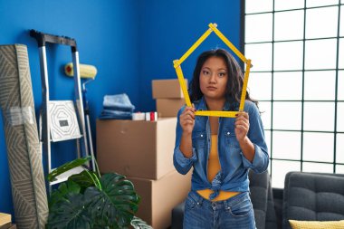 Young asian woman moving to a new home clueless and confused expression. doubt concept. 