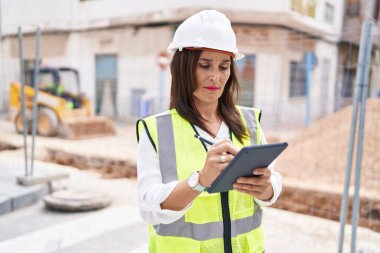 Young beautiful hispanic woman architect drawing on touchpad with relaxed expression at street