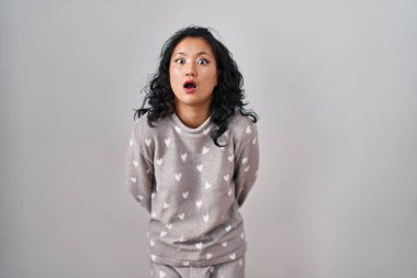 Young asian woman wearing pajama afraid and shocked with surprise expression, fear and excited face. 