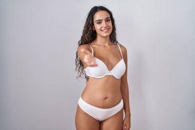 Young hispanic woman wearing white lingerie smiling cheerful offering palm hand giving assistance and acceptance. 