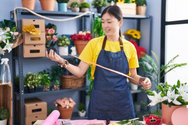 Çiçekçide dantel tutan Çinli kadın gülümsüyor.