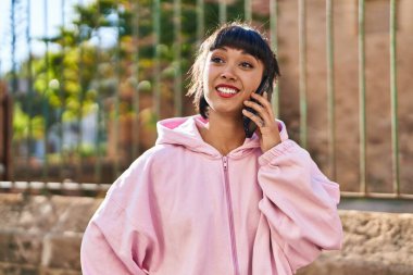 Gülümseyen genç bir kadın caddedeki akıllı telefondan konuşuyor.