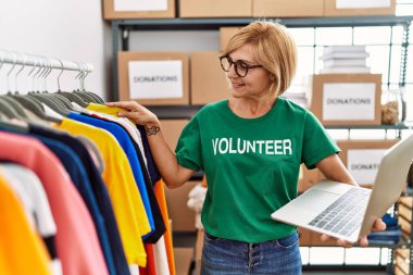 Orta yaşlı sarışın kadın gönüllü üniforması giyiyor. Yardım merkezinde çalışan dizüstü bilgisayarını kullanıyor.