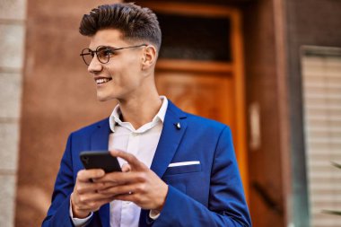 Sokakta takım elbise ve gözlük takan akıllı telefon kullanan genç adam.