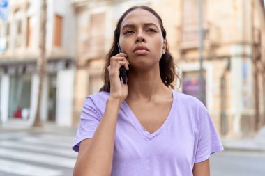 Young african american woman talking on smartphone with serious expression at street