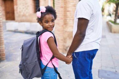 Father and daughter smiling confident walking with hands together at school