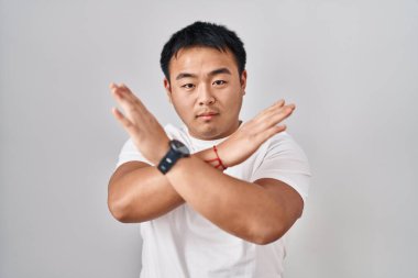 Young chinese man standing over white background rejection expression crossing arms doing negative sign, angry face 
