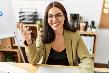 Genç, güzel, İspanyol bir iş kadını masada oturmuş ofiste konuşuyor.