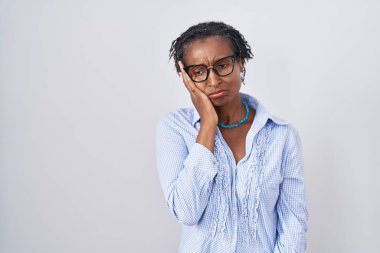 African woman with dreadlocks standing over white background wearing glasses thinking looking tired and bored with depression problems with crossed arms. 