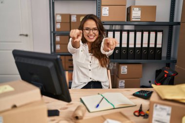 Young hispanic woman working at small business ecommerce pointing to you and the camera with fingers, smiling positive and cheerful 