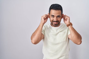 Hispanic man with beard standing over isolated background smiling pulling ears with fingers, funny gesture. audition problem 