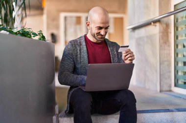 Genç adam sokakta dizüstü bilgisayar ve kredi kartı kullanıyor.