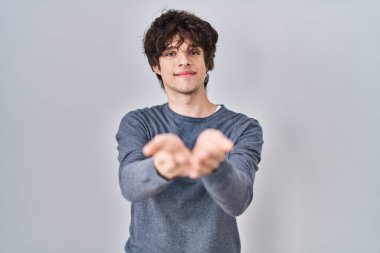 Young man standing over isolated background smiling with hands palms together receiving or giving gesture. hold and protection 