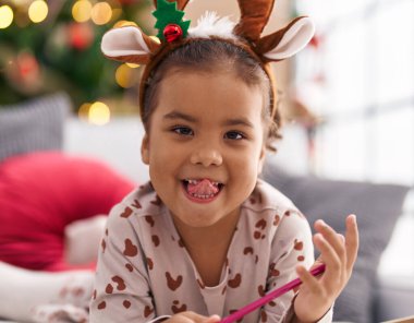 Adorable hispanic girl smiling confident lying on sofa by christmas tree at home