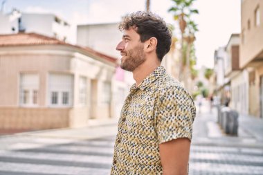 Young hispanic man standing at the street looking to side, relax profile pose with natural face with confident smile. 