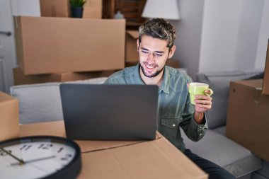 Young man using laptop drinking coffee at new home