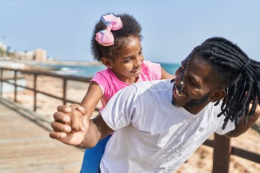 Father and daughter smiling confident holding girl on back at seaside