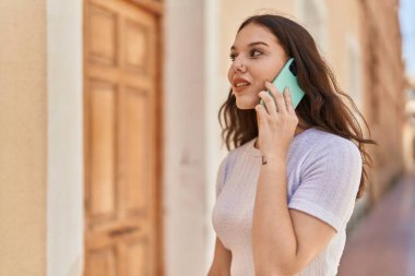 Gülümseyen genç bir kadın caddedeki akıllı telefondan konuşuyor.