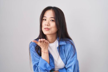 Young chinese woman standing over white background looking at the camera blowing a kiss with hand on air being lovely and sexy. love expression. 