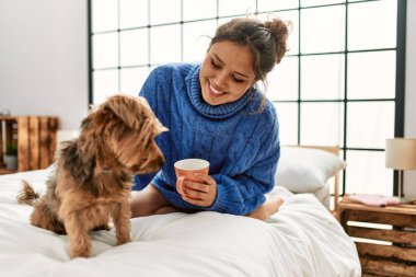 Genç, güzel, İspanyol bir kadın. Bir fincan kahve içiyor. Yatakta köpekle oturuyor.