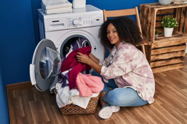 Genç Afro-Amerikan kadın gülümsüyor çamaşırhanede çamaşır yıkıyor.