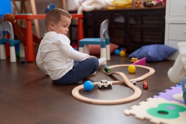 Adorable toddler playing with cars toy sitting on floor at kindergarten