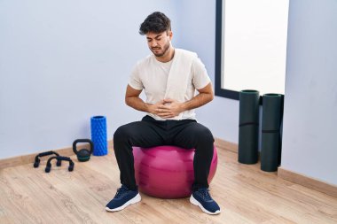 Sakallı İspanyol bir adam yoga odasında elleri karnında pilatese oturuyor çünkü mide bulantısı, acı verici bir hastalık kendini iyi hissetmiyor. Ağrı kavramı. 