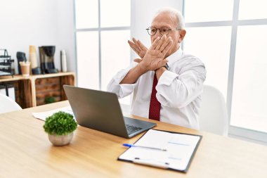 Ofiste çalışan kıdemli bir adam bilgisayarı kullanıyor. Reddetme ifadesi, kollar ve avuç içleri çapraz, kızgın yüz ifadesi. 