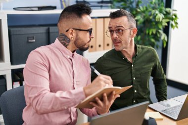 Two men business workers using laptop writing on notebook at office