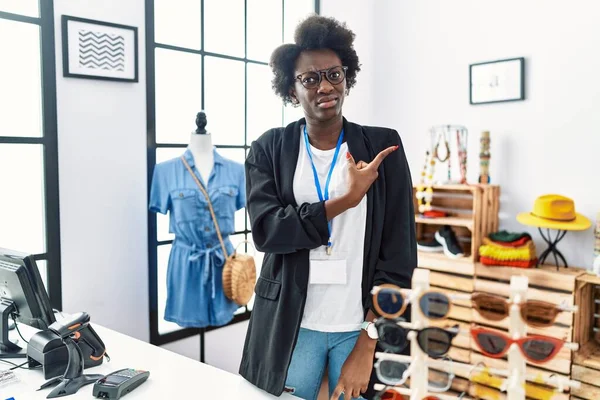 African young woman working as manager at retail boutique pointing aside worried and nervous with forefinger, concerned and surprised expression