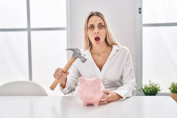 Young Blonde Woman Holding Piggy Bank Hammer Shock Face Looking — 스톡 사진