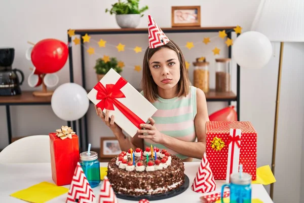 Hispanic Woman Celebrating Birthday Cake Holding Gift Relaxed Serious Expression — Stockfoto