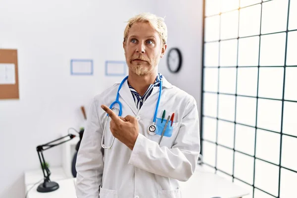 Young Blond Man Wearing Doctor Uniform Stethoscope Clinic Pointing Aside — Stock Photo, Image