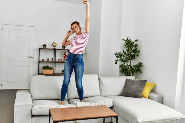Young woman listening to music and dancing standing on sofa at home