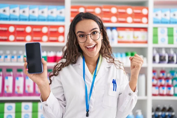 Young Hispanic Woman Working Pharmacy Drugstore Showing Smartphone Screen Shock — Foto de Stock