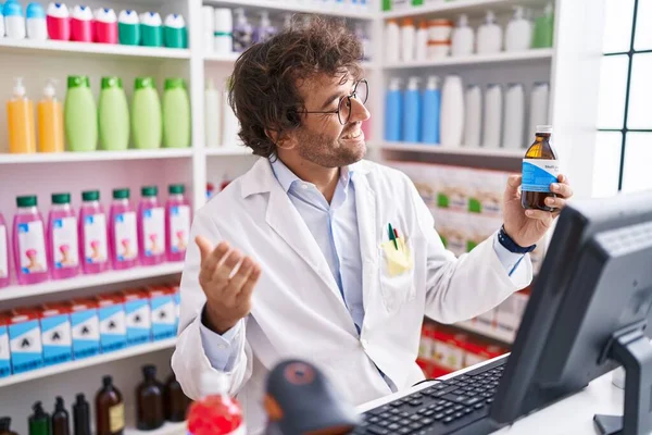 Young Hispanic Man Pharmacist Holding Medication Bottle Speaking Pharmacy — Zdjęcie stockowe