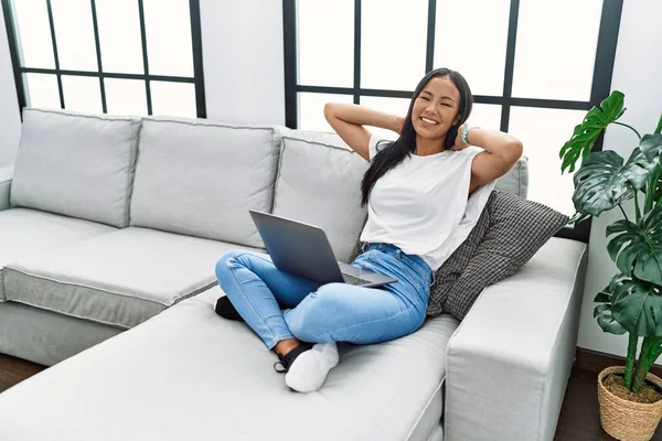 Young latin woman using laptop relaxed with hands on head at home