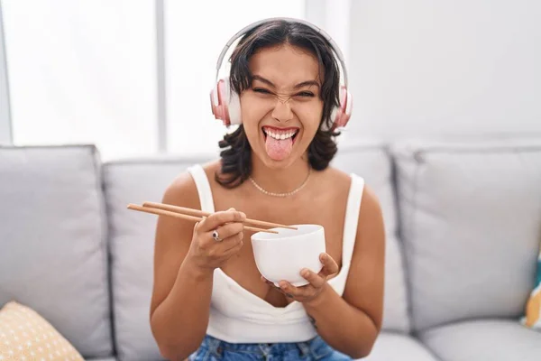 年轻的惊慌失措的女人用筷子吃着亚洲菜 伸出舌头 带着滑稽的表情高兴极了 — 图库照片