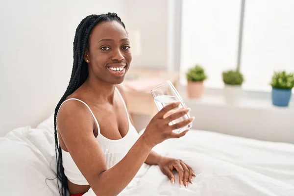 African american woman drinking water sitting on bed at bedroom