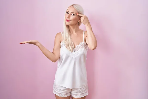 Běloška Pyžamu Oblečená Růžovém Pozadí Zmatená Otrávená Otevřenou Dlaní Ukazující — Stock fotografie