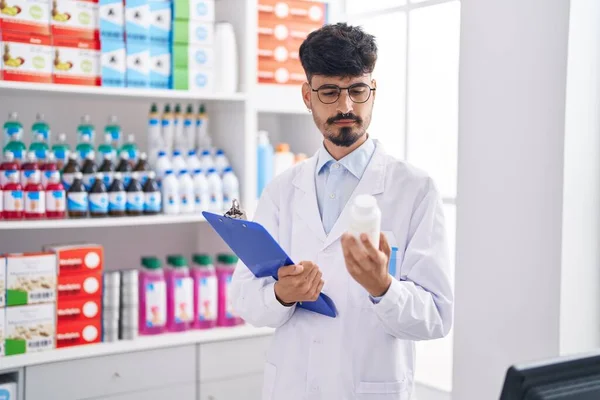 Young Hispanic Man Pharmacist Holding Pills Bottle Reading Document Pharmacy — Stok fotoğraf