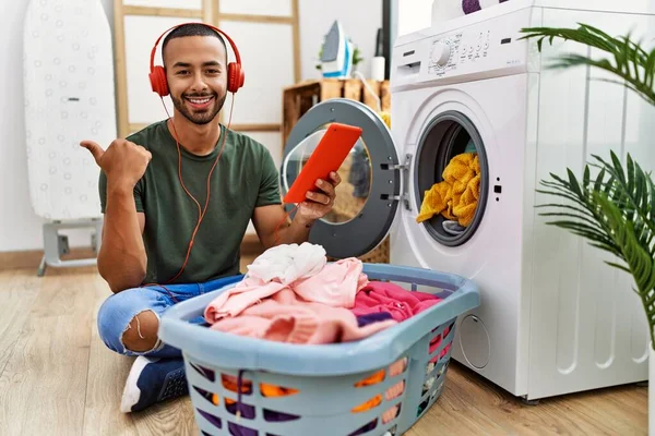 African American Man Doing Laundry Listening Music Pointing Thumb Side — Stockfoto